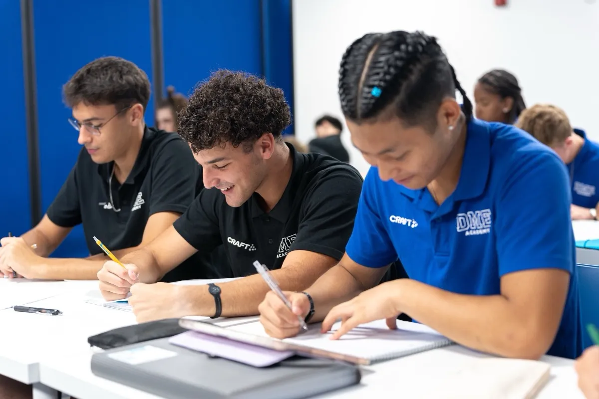 Students in DME Academy polo shirts writing at classroom desks