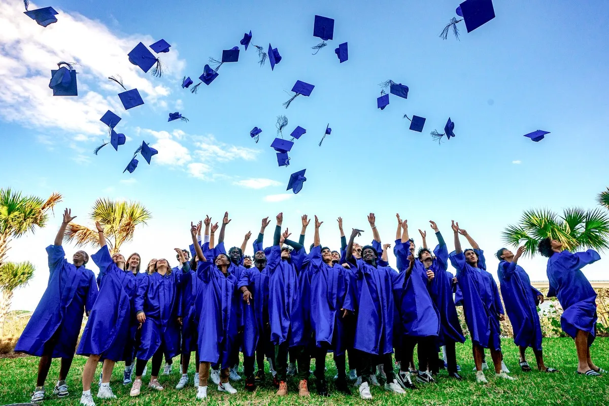 DME Academy graduates tossing caps in blue robes with palm trees