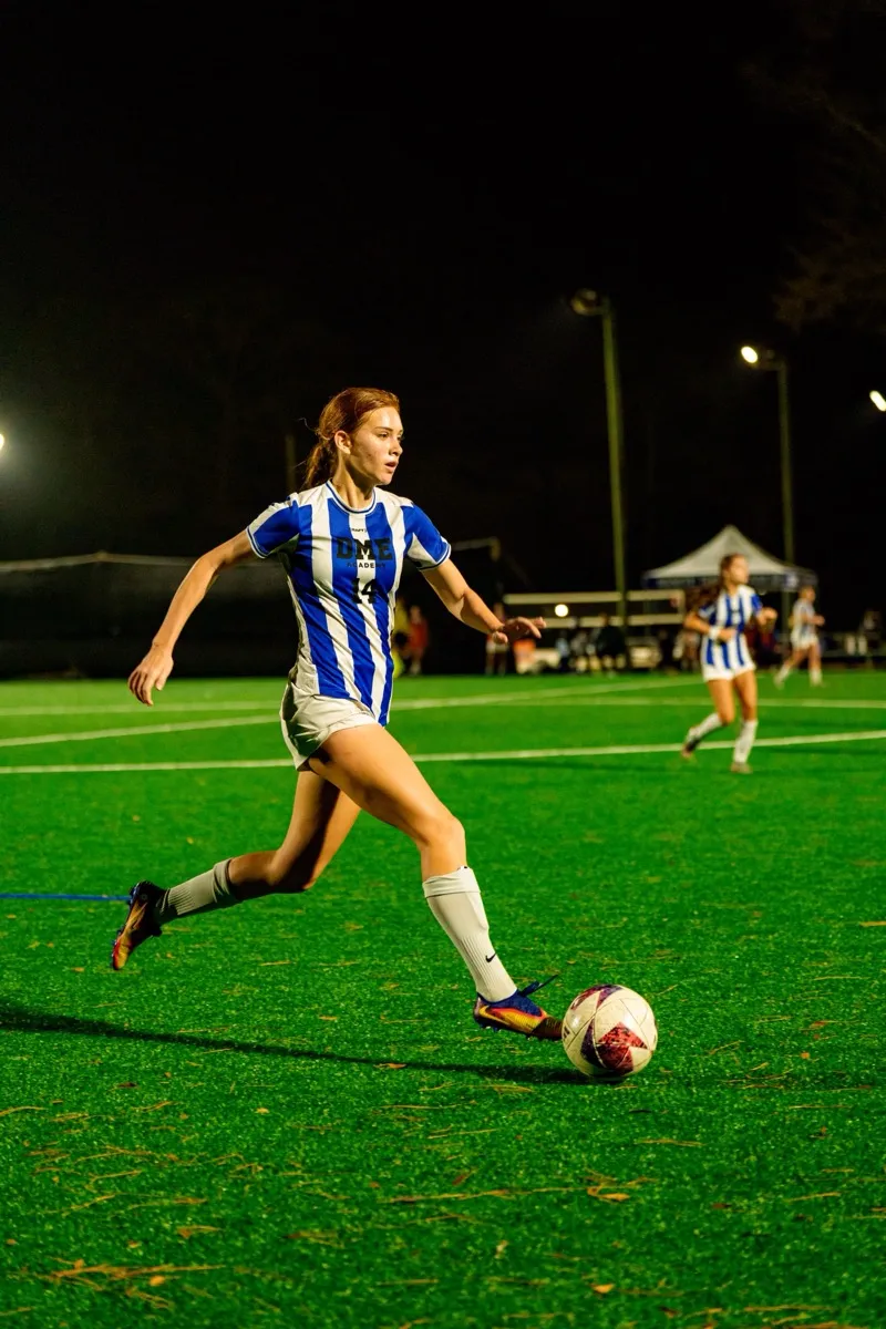 Female soccer player dribbling during night game under stadium lights